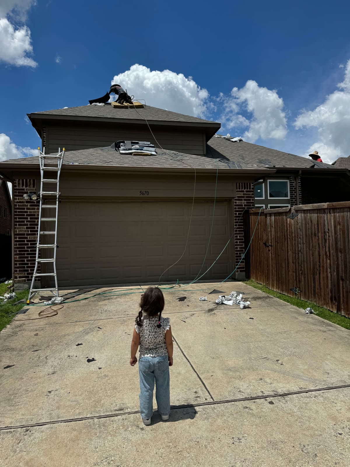 Mahmoud and Sara's daughter watching from the driveway as a Roof Raiders crew member works on the roof above