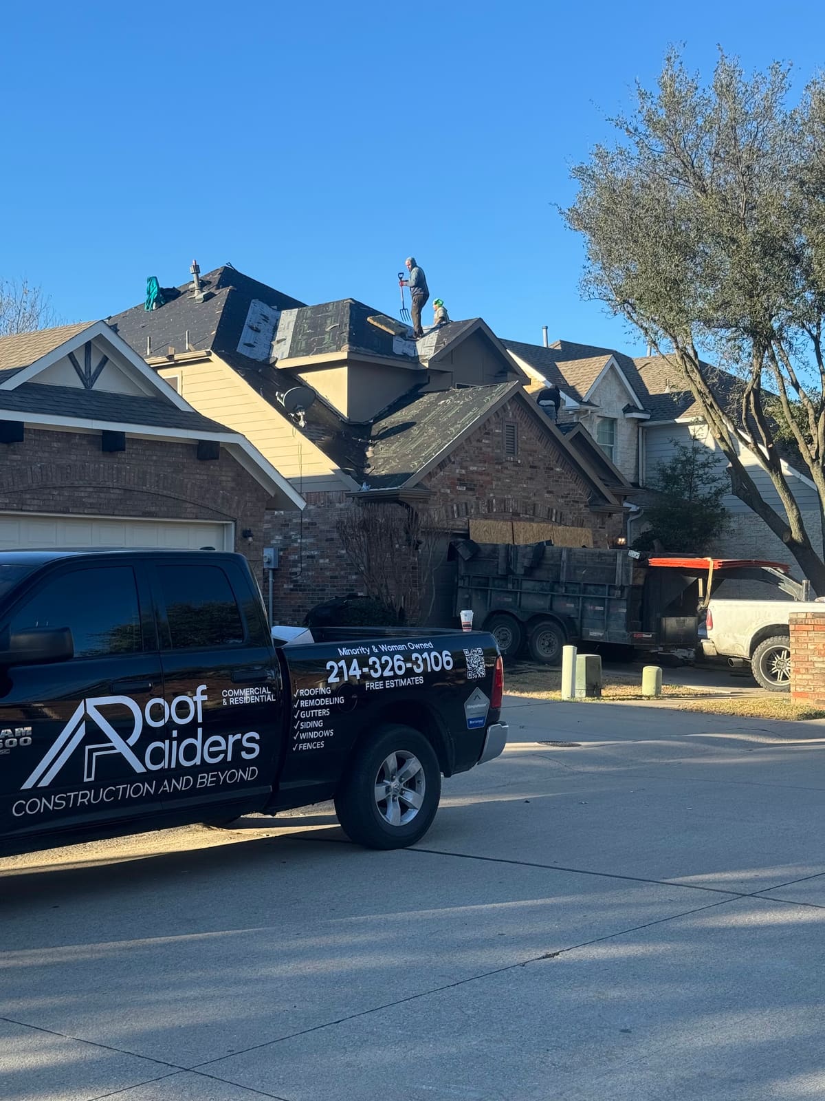 Roof Raiders crew re-roofing a two-story North Texas home with the branded company truck and dump trailer staged below