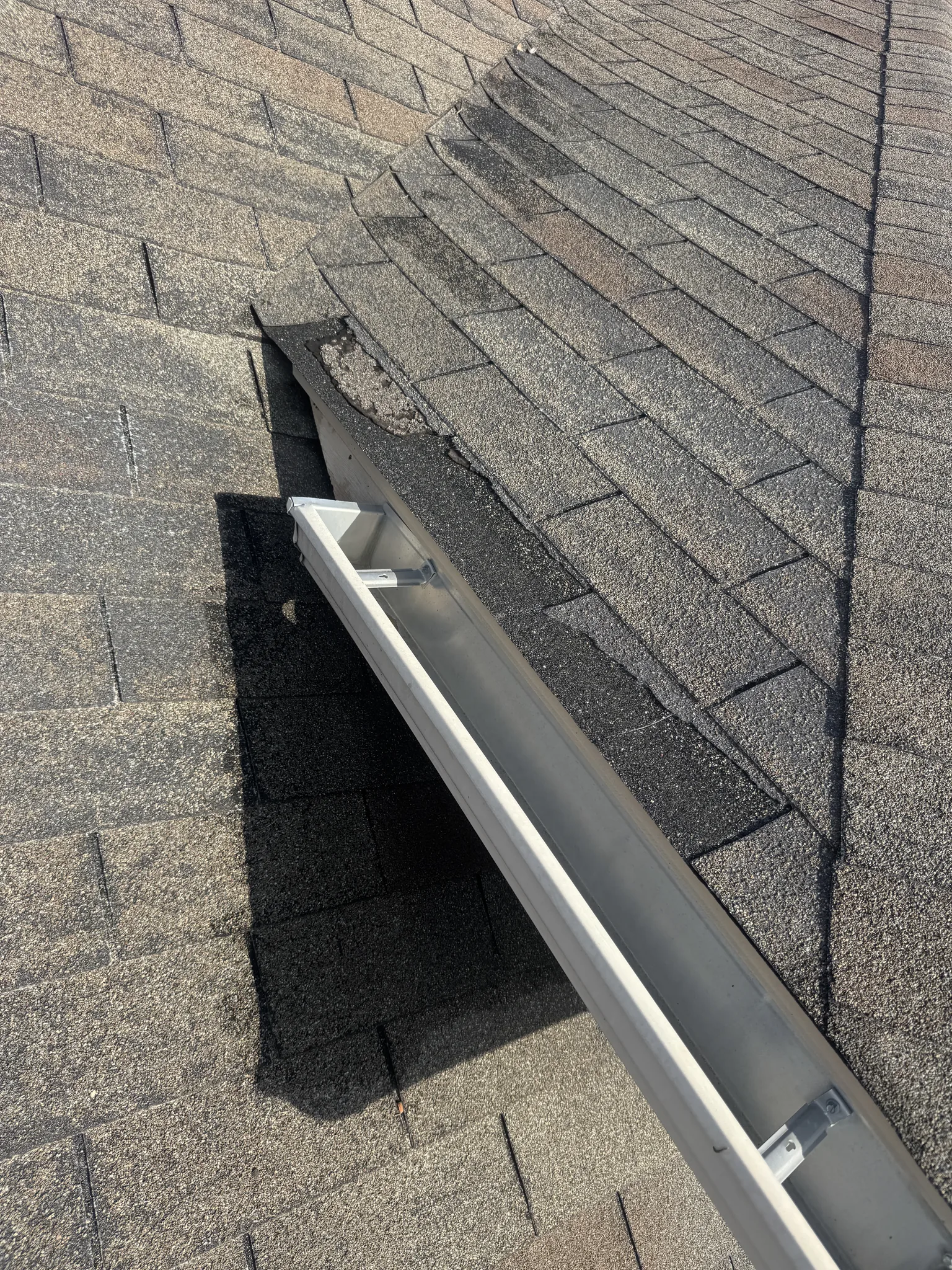 Seamless K-style aluminum gutter mounted along a North Texas roof eave with hidden hangers set into the fascia where two shingle faces meet