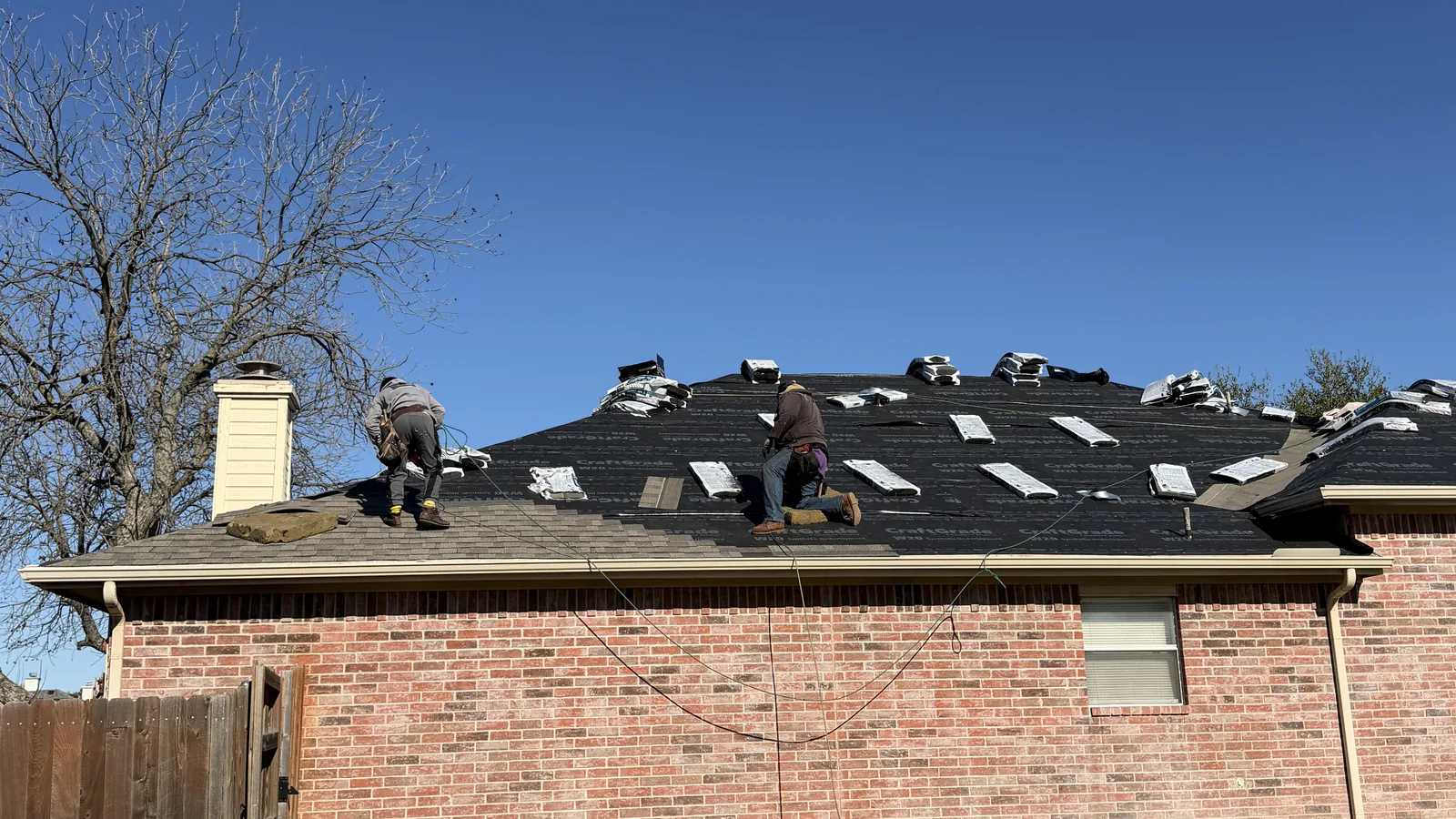 Roof Raiders crew tearing off a hail-damaged shingle roof on a Plano, TX brick home