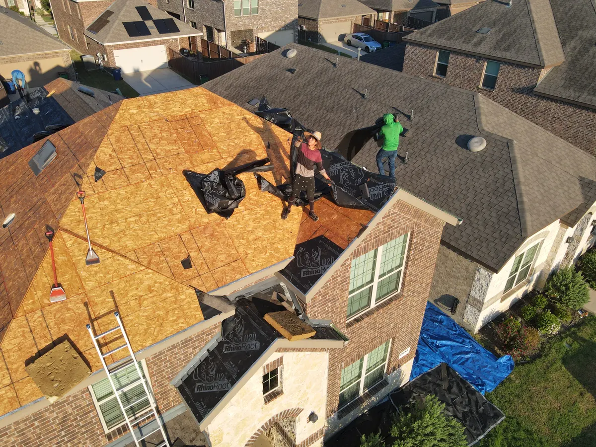 Close drone view of two Roof Raiders crew members laying underlayment during a roof repair on a North Texas home
