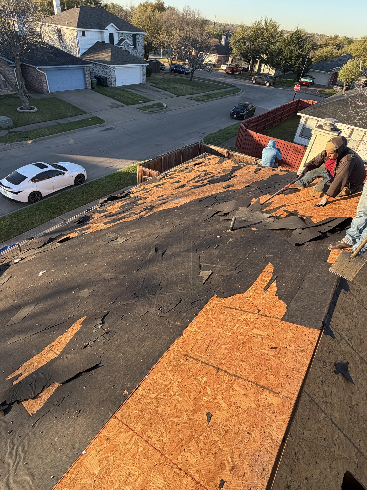 Roof Raiders crew working a storm-damaged slope, pulling failed shingles down to the felt and decking on a North Texas home