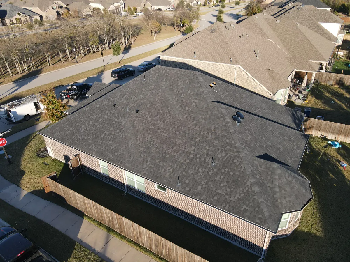 Aerial view of a completed architectural shingle roof replacement by Roof Raiders on a North Texas home, with company trucks parked at the curb