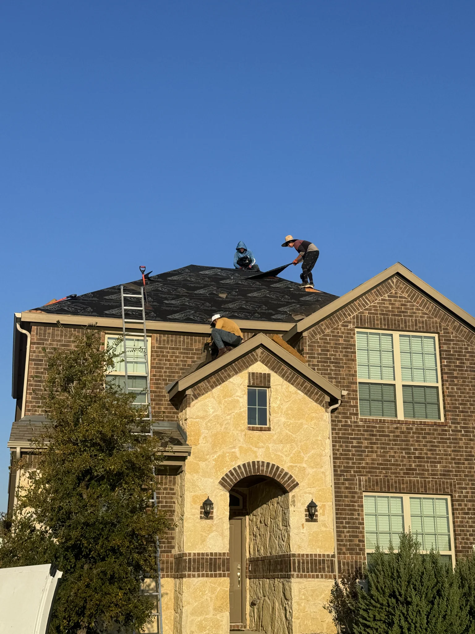 A roofing crew installing architectural asphalt shingles on a two-story North Texas brick home