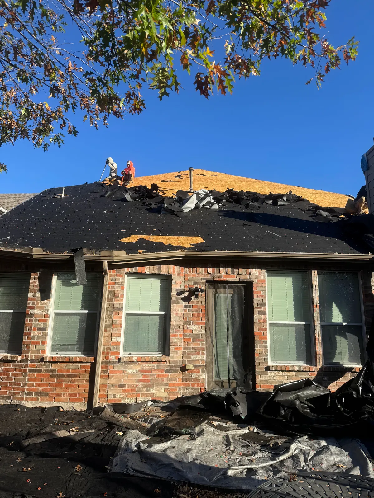 Roof Raiders crew working at the ridge during a full tear-off with the old shingles stripped and felt exposed on a North Texas home