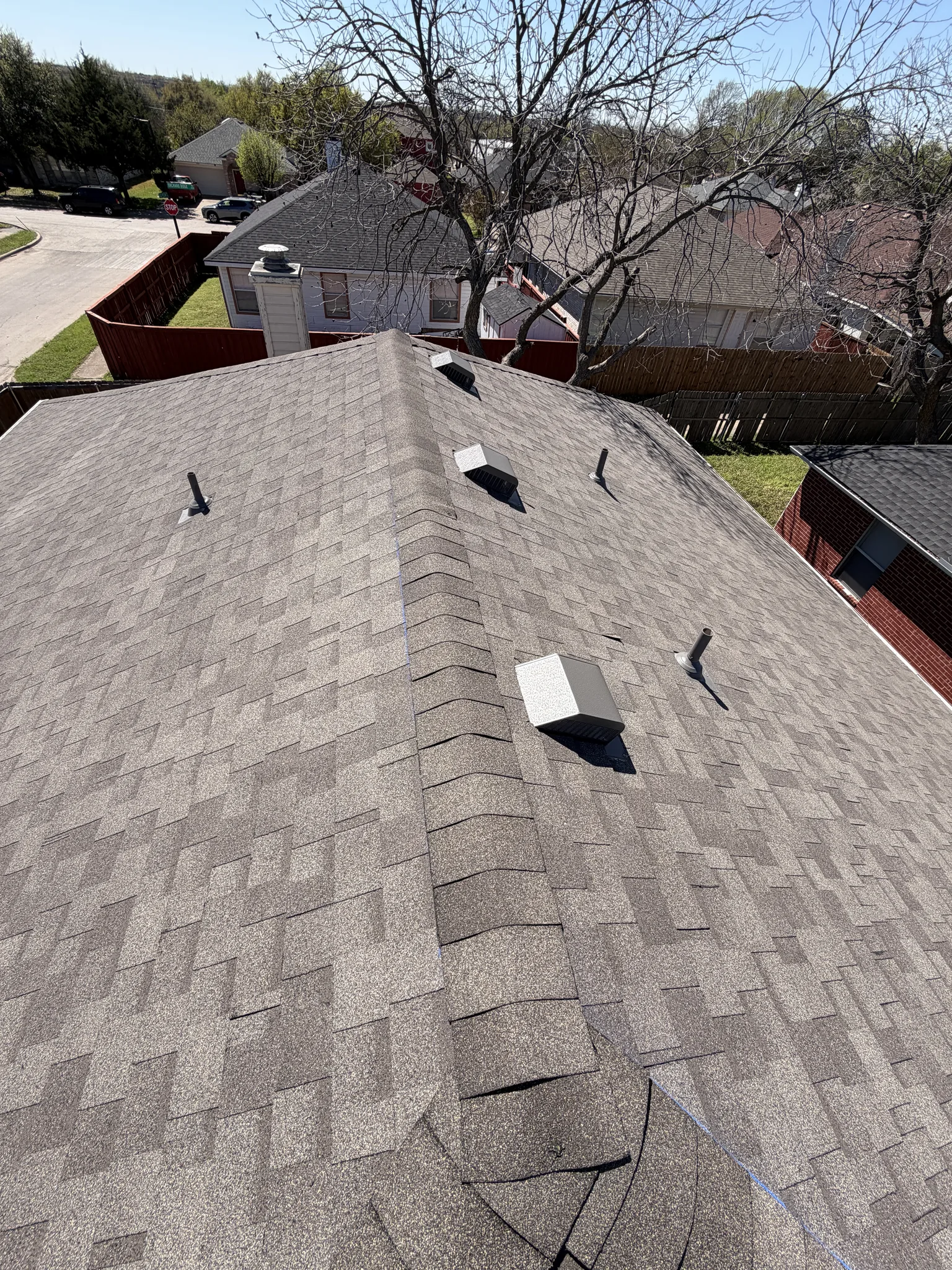 Architectural asphalt shingle roof on a two-story North Texas brick home, with box vents and pipe penetrations along the ridge
