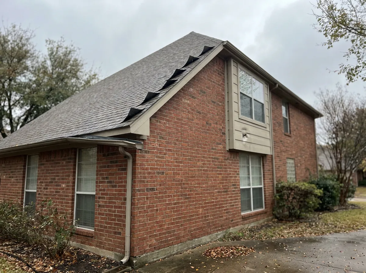A single home elevation showing wind-damaged roof, dented gutters, and siding impact from a storm